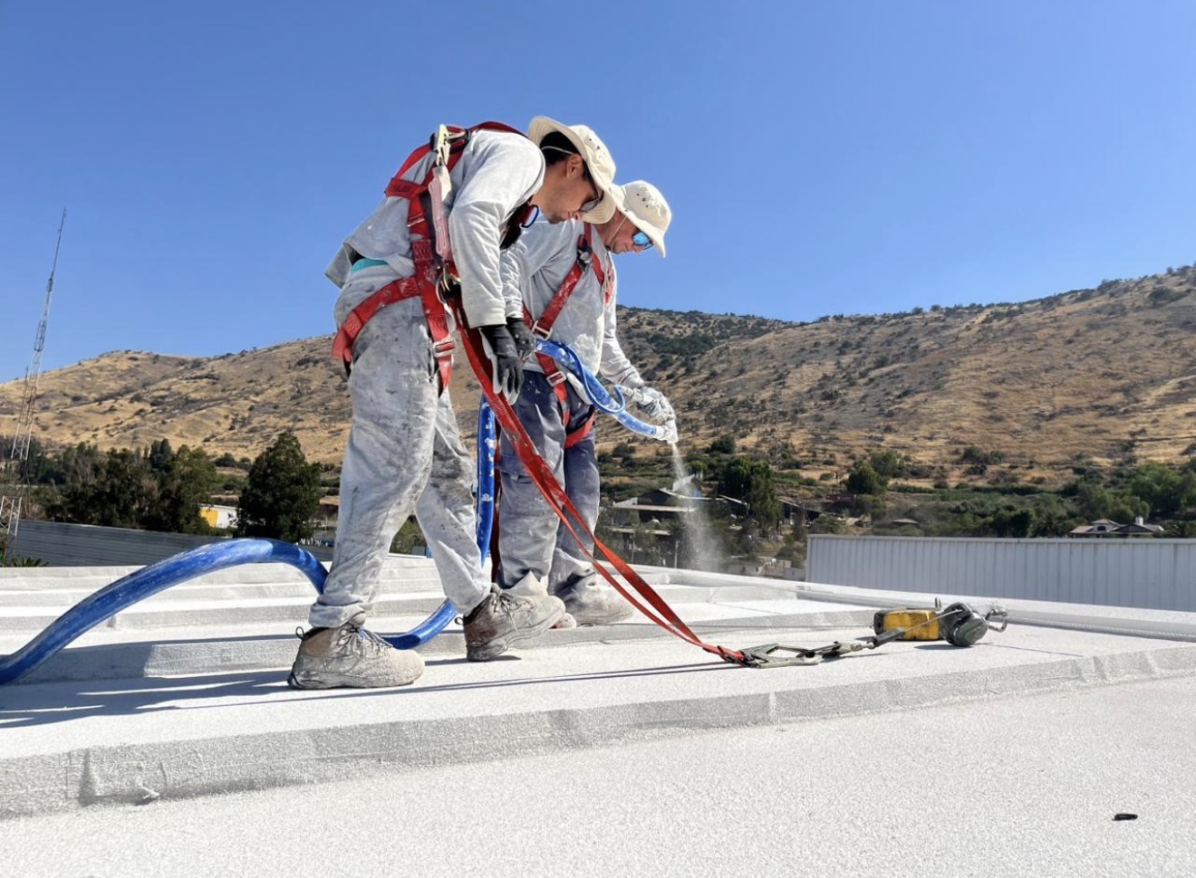 Applicators in fall-arrest harnesses spraying cork on a roof deck