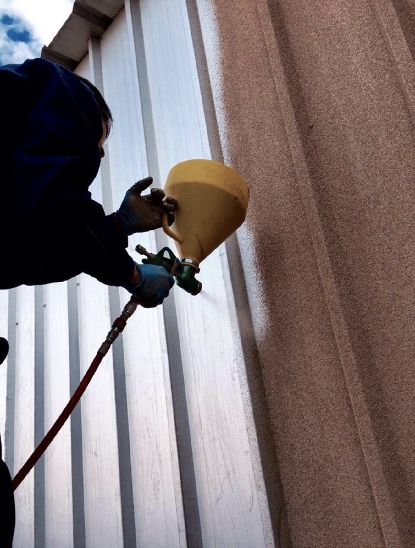 Spray cork being applied to profiled metal cladding with a hopper gun